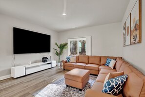 Una sala de estar moderna con un televisor de pantalla plana grande, un sofá de cuero, un mueble de entretenimiento blanco y una alfombra estampada.