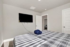 Une chambre à coucher avec un lit, un téléviseur fixé au mur et une porte donnant sur une autre pièce.