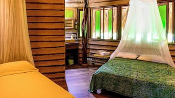 A room with a bed under a canopy, a small table with a chair, and a window with green-tinted glass.