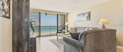 A living room with a grey sofa, two lamps, a painting, and a view of the beach.