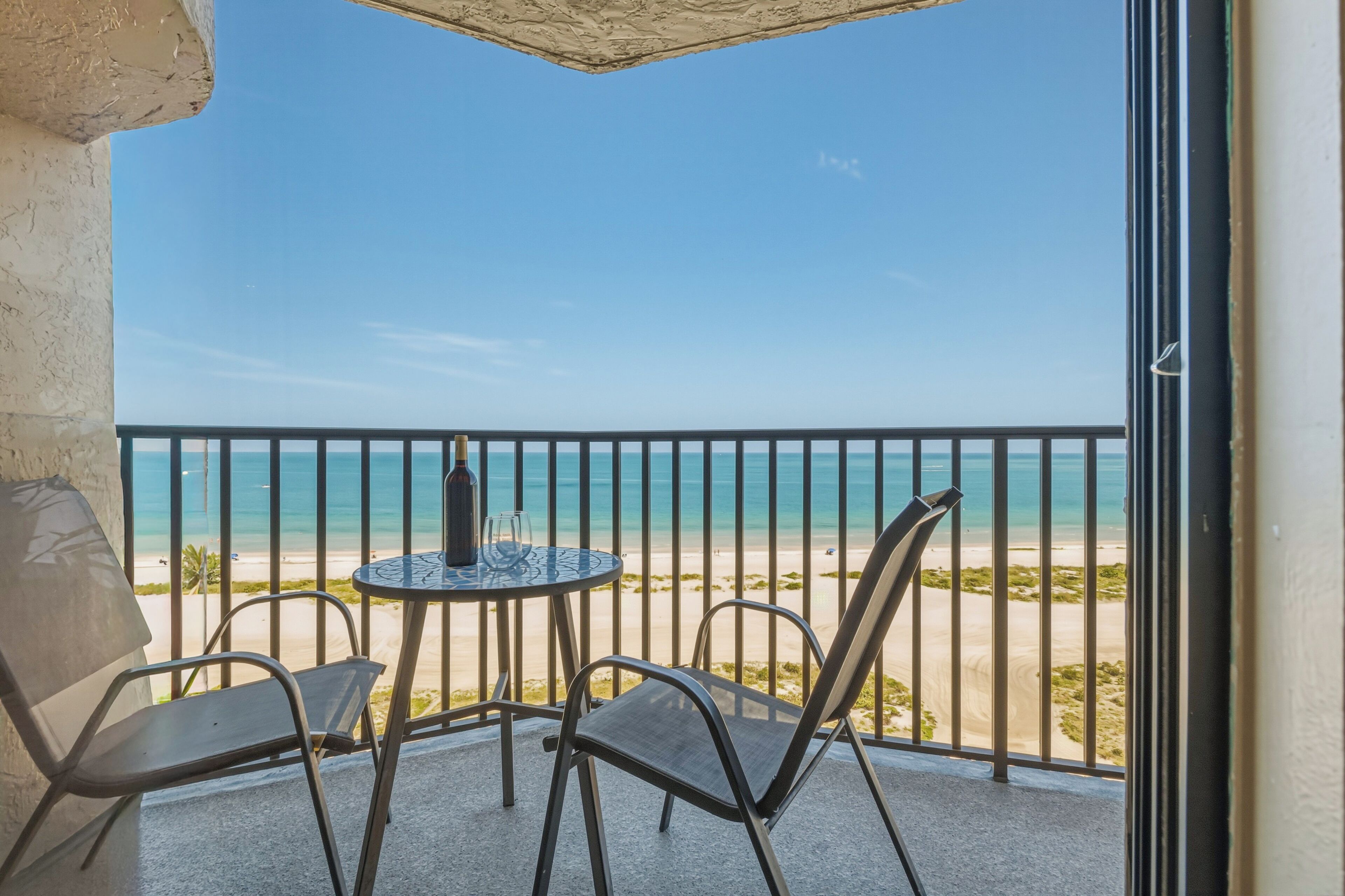 A balcony with a table and chairs, overlooking a beach.
