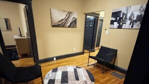 A room with a wooden floor, a round table, two black chairs, and two abstract paintings on the walls.