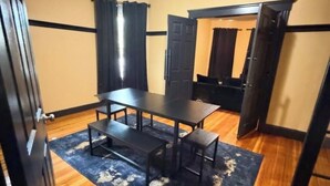 A room with a wooden floor, a dark rug, a table with benches, and a door.