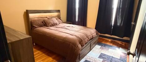 A bedroom with a bed, a wooden floor, a patterned rug, and a door with a handle.