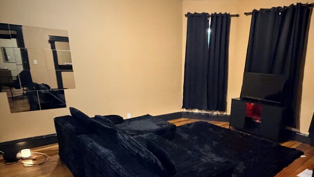 A room with a black sofa, a television, a mirror, and a ceiling light.