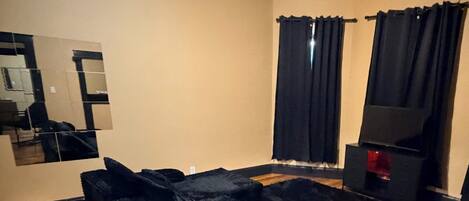 A room with a black sofa, a television, a mirror, and a ceiling light.