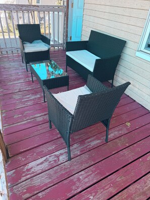 A wooden deck with wicker furniture, including a sofa and chairs, and a glass-top coffee table.