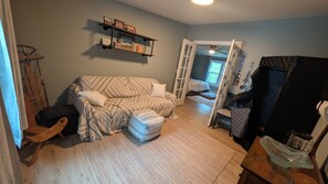 Ein gemütliches Zimmer mit einer Couch, Hocker, einem Holzschaukelstuhl und einem Bett im Hintergrund.