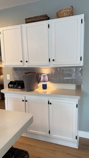 A kitchen with white cabinets, a countertop, a blue lamp, and a woven basket. - Cozy County Cottage- Pet friendly (Afton)