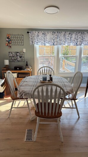 A dining area with a table set for four, surrounded by white chairs with wooden seats. - Cozy County Cottage- Pet friendly (Afton)