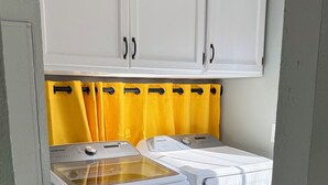 A laundry area with two white washing machines, a yellow curtain, and a grey carpet. - Cozy County Cottage- Pet friendly (Afton)