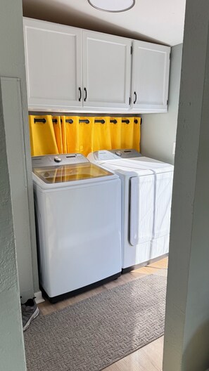 Ein Waschbereich mit zwei weißen Waschmaschinen, einem gelben Vorhang und einem grauen Teppich.