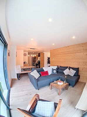 Ein modernes Wohnzimmer mit einer Eckcouch, einer Wand aus Holzvertäfelung und einem Essbereich im Hintergrund.