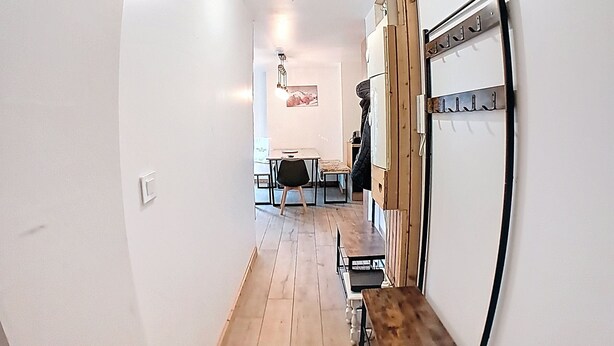 Un pasillo con suelo de madera, un perchero y una zona de comedor al fondo.