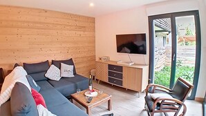 Una sala de estar moderna con un sofá seccional, un mueble de madera, un televisor de pantalla plana y una puerta de vidrio que da a un espacio exterior.