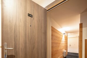 A hotel room with a wooden door, a visible room number sign, and a corner with a light fixture. - travelski home premium - Résidence La Mariande - 3 Pièces 6 personnes N°0.3 (Les Deux Alpes)
