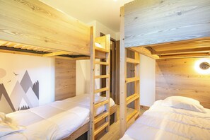 Quarto com beliche, cabeceira de madeira e escada, roupa de cama branca e parede com desenho de montanhas.