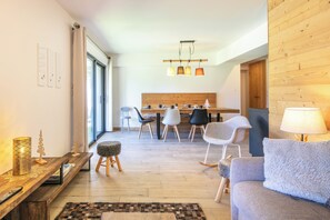 A modern living room with a sofa, a coffee table, and a dining area with chairs and a wooden headboard. - travelski home premium - Résidence La Mariande - 3 Pièces 6 personnes N°0.3 (Les Deux Alpes)
