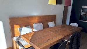 Puisesta ruokapöydästä ja neljästä tuolista koostuva ruokailuryhmä, pehmustettu penkki sekä moderni keittiö, jossa on mikroaaltouuni ja uuni.