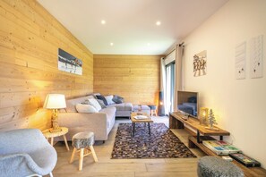 A modern living room with a wooden wall, a sofa, a coffee table, a TV, and a patterned rug. - travelski home premium - Résidence La Mariande - 3 Pièces 6 personnes N°0.3 (Les Deux Alpes)