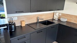 Moderni keittiö, jossa on tummat kaapit, musta työtaso, pesuallas, leivänpaahdin ja kahvinkeitin.