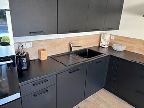 Eine moderne Küche mit dunklen Schränken, einer schwarzen Arbeitsplatte, einem Spülbecken, einem Toaster und einer Kaffeemaschine.
