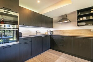 A modern kitchen with dark cabinetry, stainless steel appliances, and a wooden backsplash. - travelski home premium - Résidence La Mariande - 3 Pièces 6 personnes N°0.3 (Les Deux Alpes)