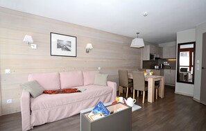 A modern living room with a sofa, a dining area with chairs, a kitchen with a microwave, and a large mirror. - travelski home select - Résidence Le Panoramic - 2 Pièces 4 personnes (Arâches-la-Frasse)