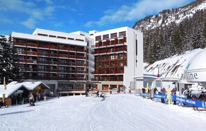 A ski resort with a large building featuring multiple balconies, a ski lift, and a snowy mountain backdrop. - travelski home select - Résidence Le Panoramic - 2 Pièces 4 personnes (Arâches-la-Frasse)