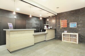 A reception desk with a wooden finish, a stone wall, and a small shelf with brochures. - travelski home select - Résidence Le Panoramic - 2 Pièces 4 personnes (Arâches-la-Frasse)