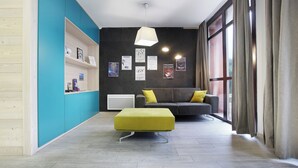 Ein modernes Wohnzimmer mit einer Couch, einem grünen Hocker und einer Wand mit gerahmten Bildern.