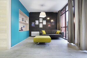 A modern living room with a sofa, a green ottoman, and a wall with framed pictures. - travelski home select - Résidence Le Panoramic - 2 Pièces 4 personnes (Arâches-la-Frasse)