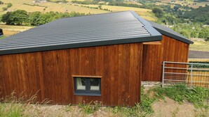 Een houten gebouw met een metalen dak, een klein raam en een metalen hek.