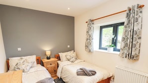 Een slaapkamer met twee bedden, een nachtkastje met een lamp, een raam met gordijnen en een radiator.