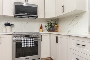 A kitchen with white cabinets, a stainless steel oven, and a microwave. - 5BR Luxe Retreat in Runaway Bay ~ Private Pool ~ Beach Access (Runaway Bay)