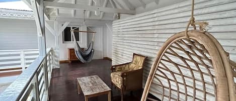 Uma área externa coberta com uma rede, uma cadeira de vime e uma mesa de madeira.
