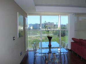 Een modern interieur met een eettafel en stoelen, een rode bank en grote ramen met uitzicht op gebouwen en groen.