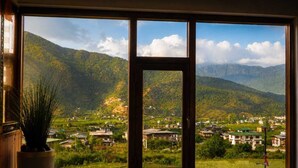 A room with a large window overlooking a mountainous landscape with buildings. - Hotel River Valley Paro (Paro)