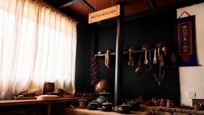 A traditional kitchen with a sign reading 'Bhutan Kitchen,' featuring a stove, pots, and utensils. - Hotel River Valley Paro (Paro)