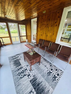 A wooden-paneled room with a large window, a bench, a table with a vase, and a patterned rug.