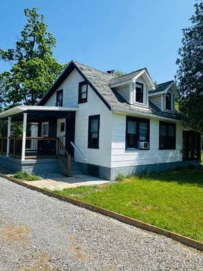 A two-story house with a covered porch, a front entrance with a staircase, and a well-maintained lawn.