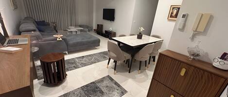 A modern living room with a sofa, a dining table with chairs, a TV mounted on the wall, and a wooden cabinet.