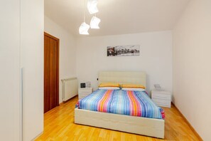 Une chambre à coucher comprenant un lit, des tables de chevet, un radiateur, une porte et un luminaire suspendu.