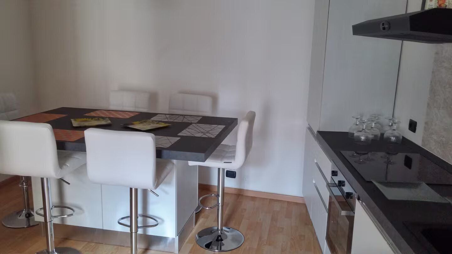 Een moderne keuken met een eethoek, inclusief een tafel met stoelen, een aanrecht met spoelbak en een afzuigkap boven het fornuis.