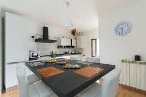 A modern kitchen with white cabinets, a black countertop, and a dining table with orange placemats. - Francesca Relax Apartment, a two-minute walk from Piazza Lago and downtown (Como)