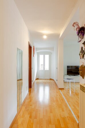 A hallway with wooden flooring, white walls, and a door leading to a room with a television. - Francesca Relax Apartment, a two-minute walk from Piazza Lago and downtown (Como)
