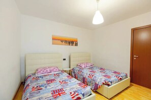 A bedroom with two beds, a small round table, a painting on the wall, and a wooden door. - Francesca Relax Apartment, a two-minute walk from Piazza Lago and downtown (Como)