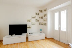 Une pièce avec un téléviseur à écran plat posé sur un meuble blanc, un petit globe terrestre et un mur décoré de photographies en noir et blanc.