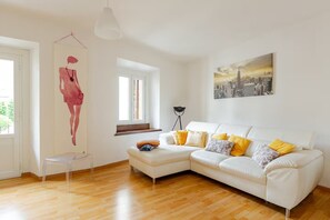 A modern living room with a white sofa, wooden flooring, a cityscape painting, and a sculpture. - Francesca Relax Apartment, a two-minute walk from Piazza Lago and downtown (Como)