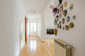 Un couloir avec un plancher en bois, un mur blanc orné d’une rangée de masques, une porte blanche et un radiateur blanc.
